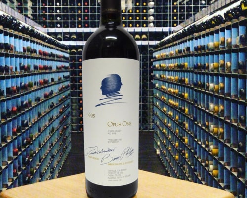 A bottle of Opus One wine stands in a modern wine cellar lined with shelves of assorted wine bottles, all organized inside safe & secure wine racks.