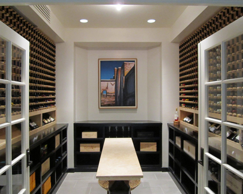 Modern wine cellar featuring wine racks for wine collectors, shelves of wine bottles, a central table, and a framed artwork on the back wall